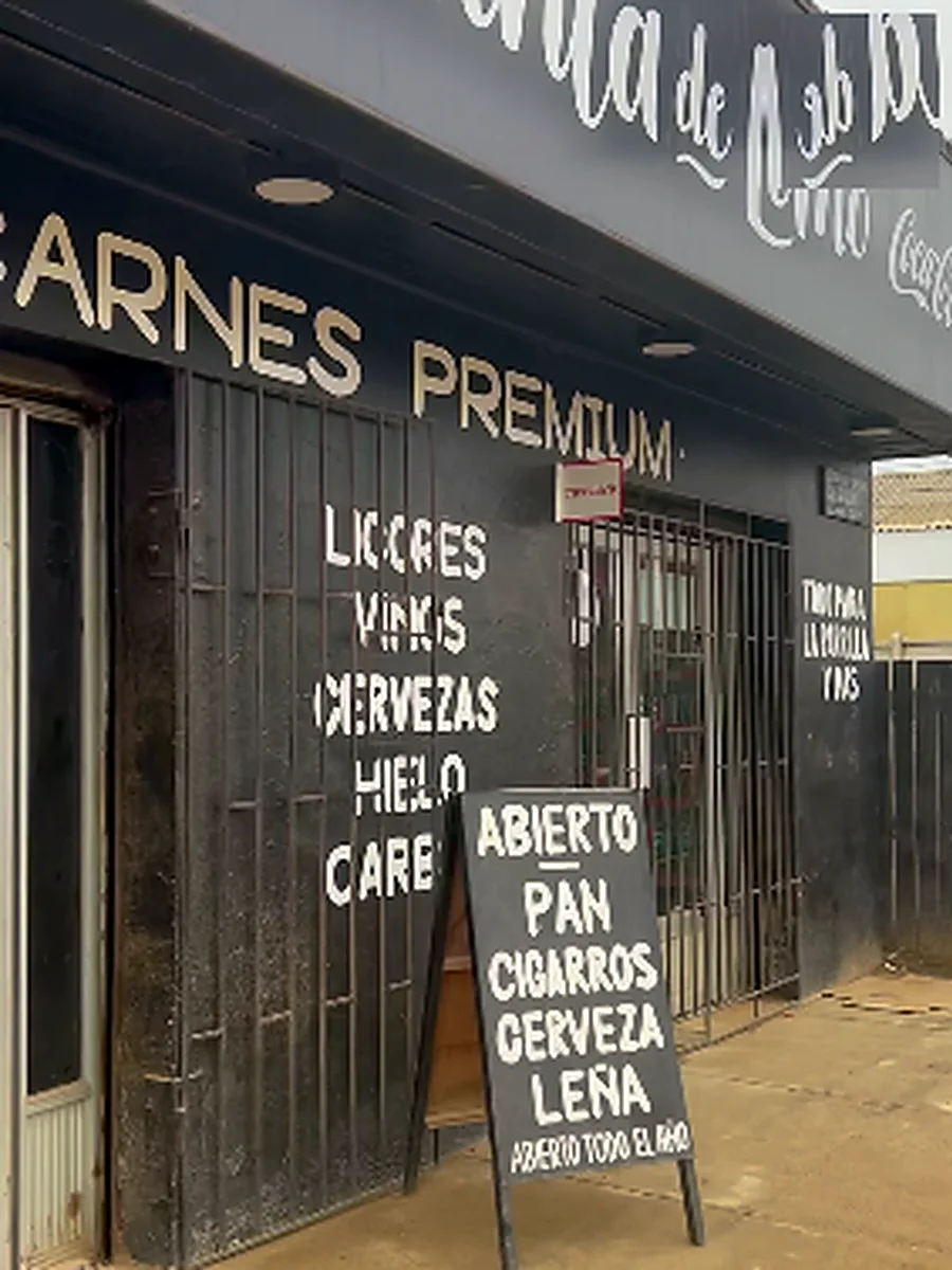 Letrero del local con la lista de productos: licores, vinos, cervezas, hielo, carbón, pan y leña
